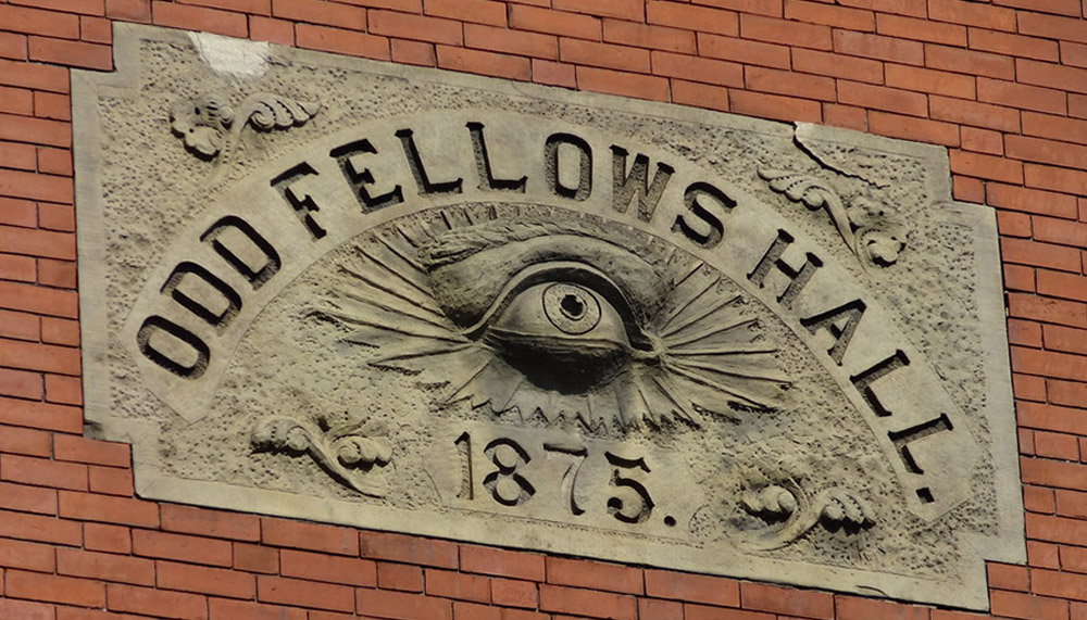 A relief carving showing an eye surrounded by the words Odd Fellows Hall, 1875 on the side of a brick building.  